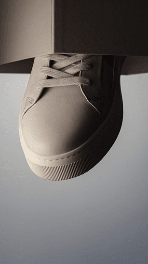 A cream leather sneaker suspended against a grey backdrop