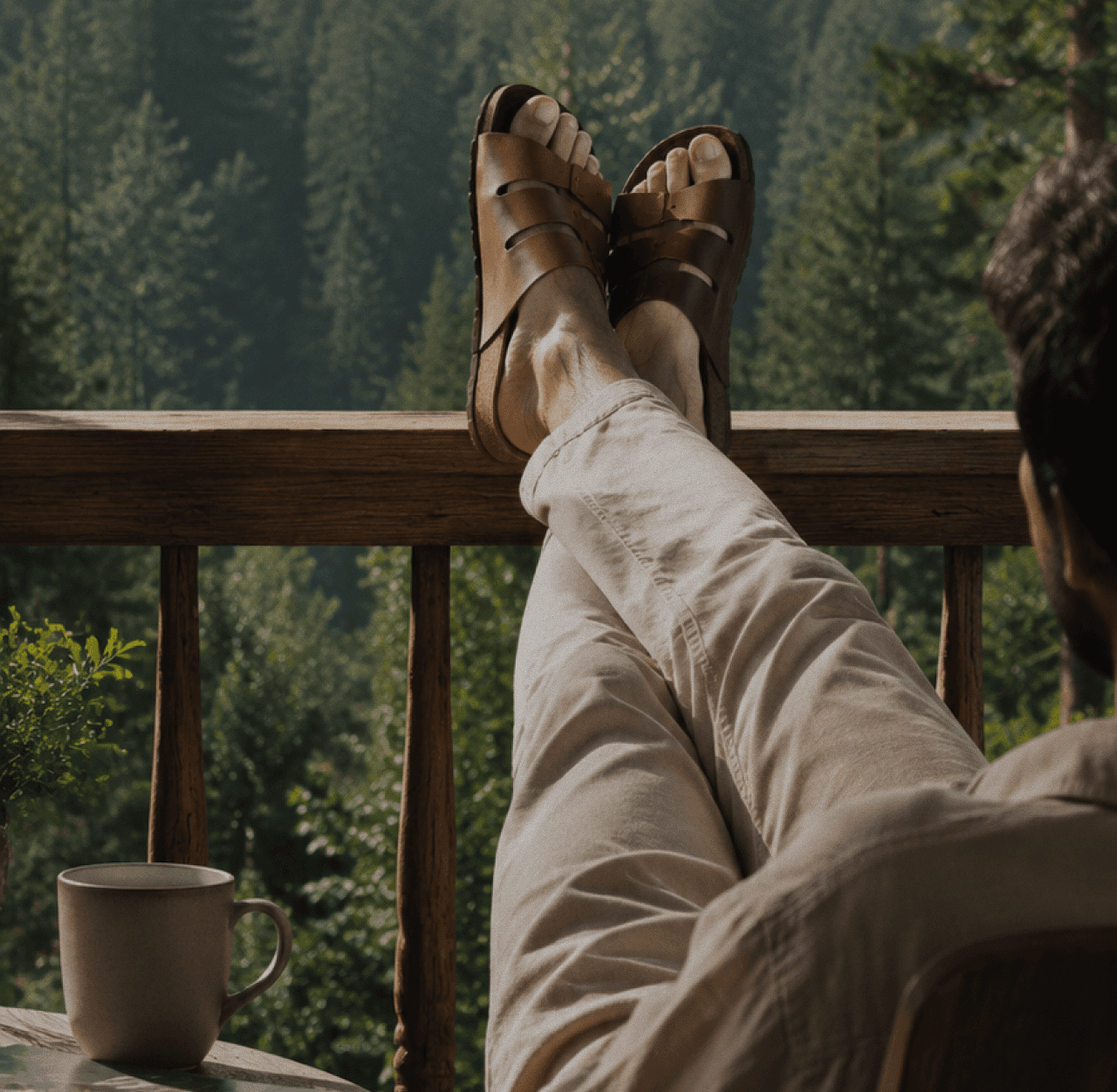 A man resting with his feet up on a cabin railing, wearing leather Kaalcari sandals